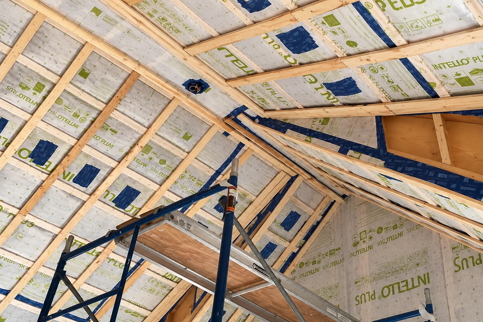 Attic rafters covered with printed white membrane panels, with a blue work platform below.