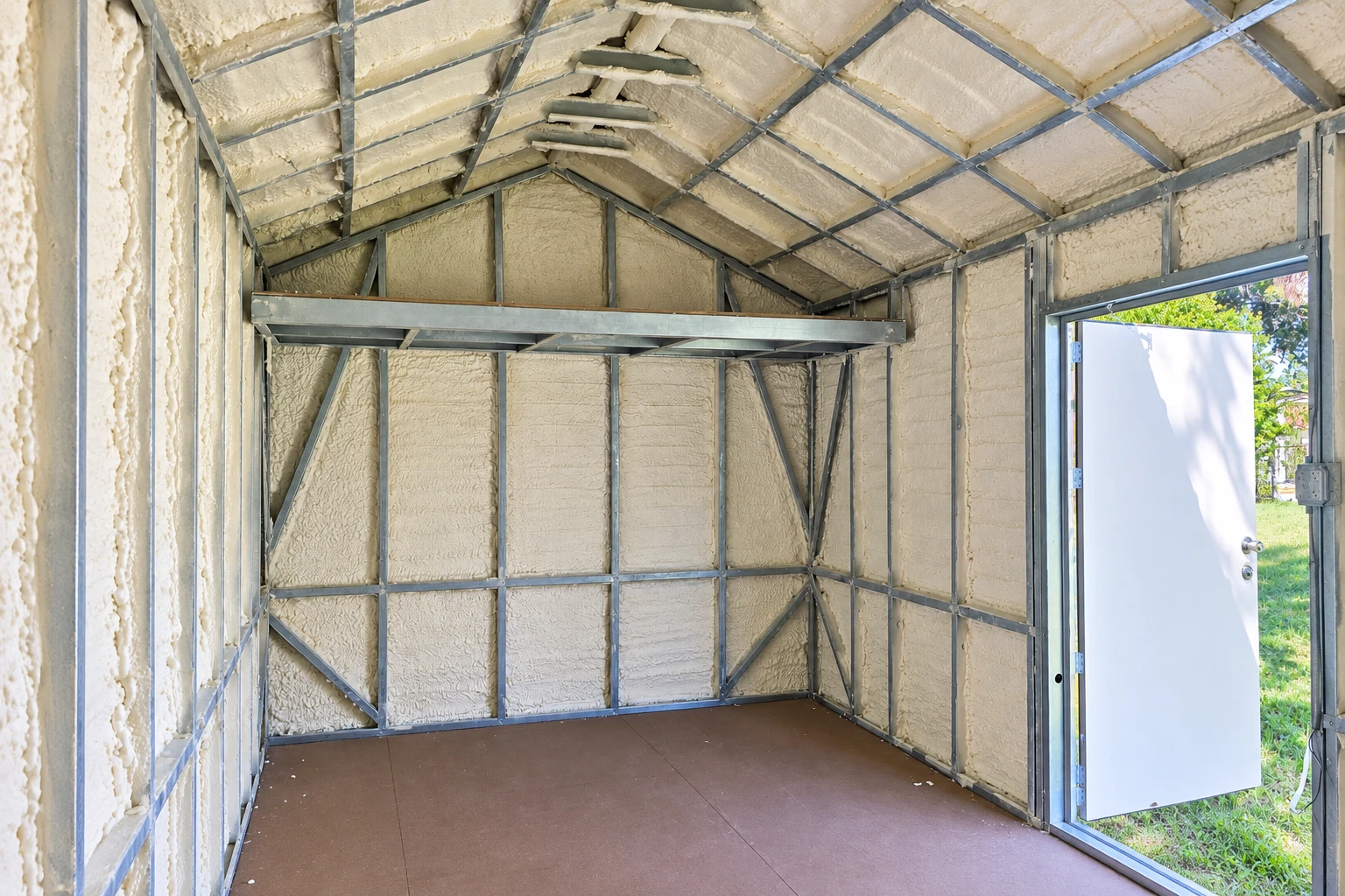 A commercial space with cream-colored spray foam covering the walls and pitched ceiling between exposed metal framing.
